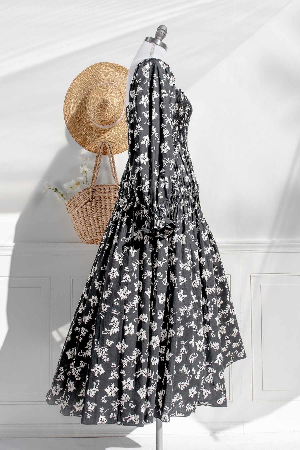 Black floral dress on a mannequin with a straw hat and wicker bag against a white background