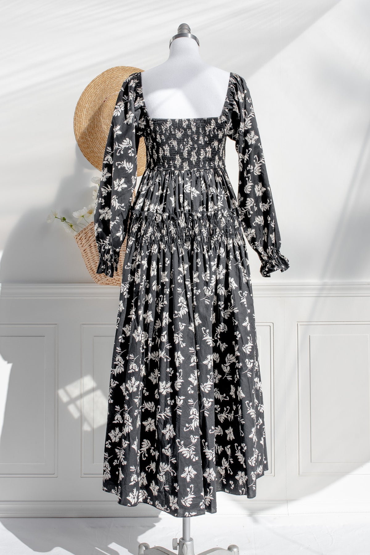 Black floral dress on a mannequin with a straw hat in a white room.