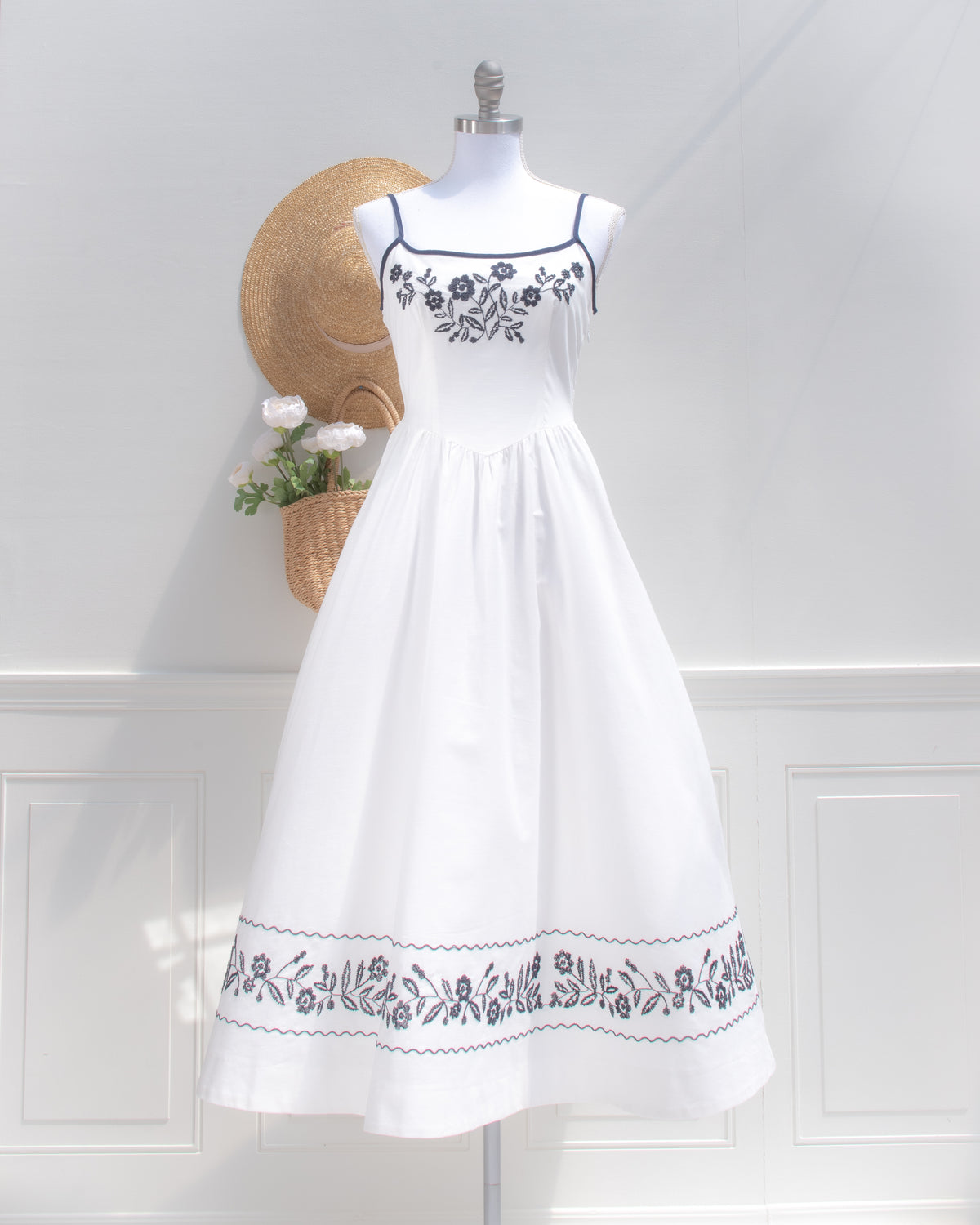 Front view of the Celeste dress, a vintage-inspired white embroidered midi dress with navy trim and a fitted bodice.