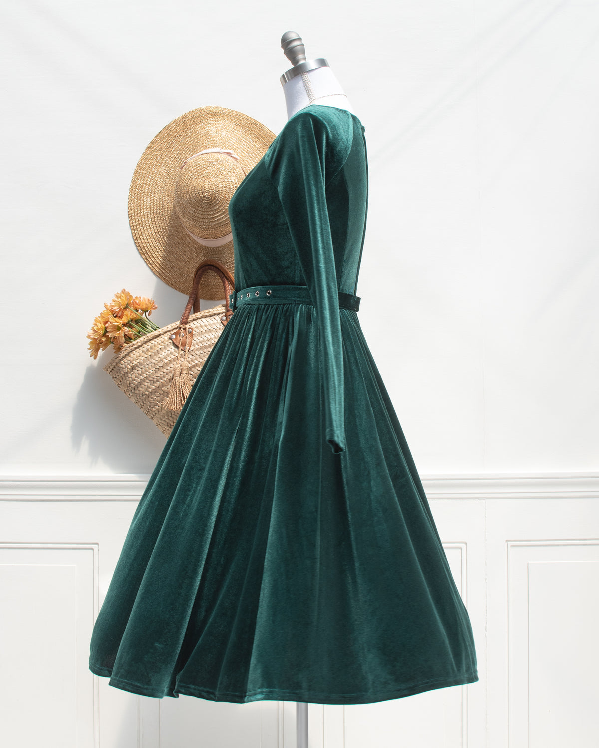 Side view of the emerald velvet dress, showing the long sleeve, belted waist and full gathered skirt flaring out.