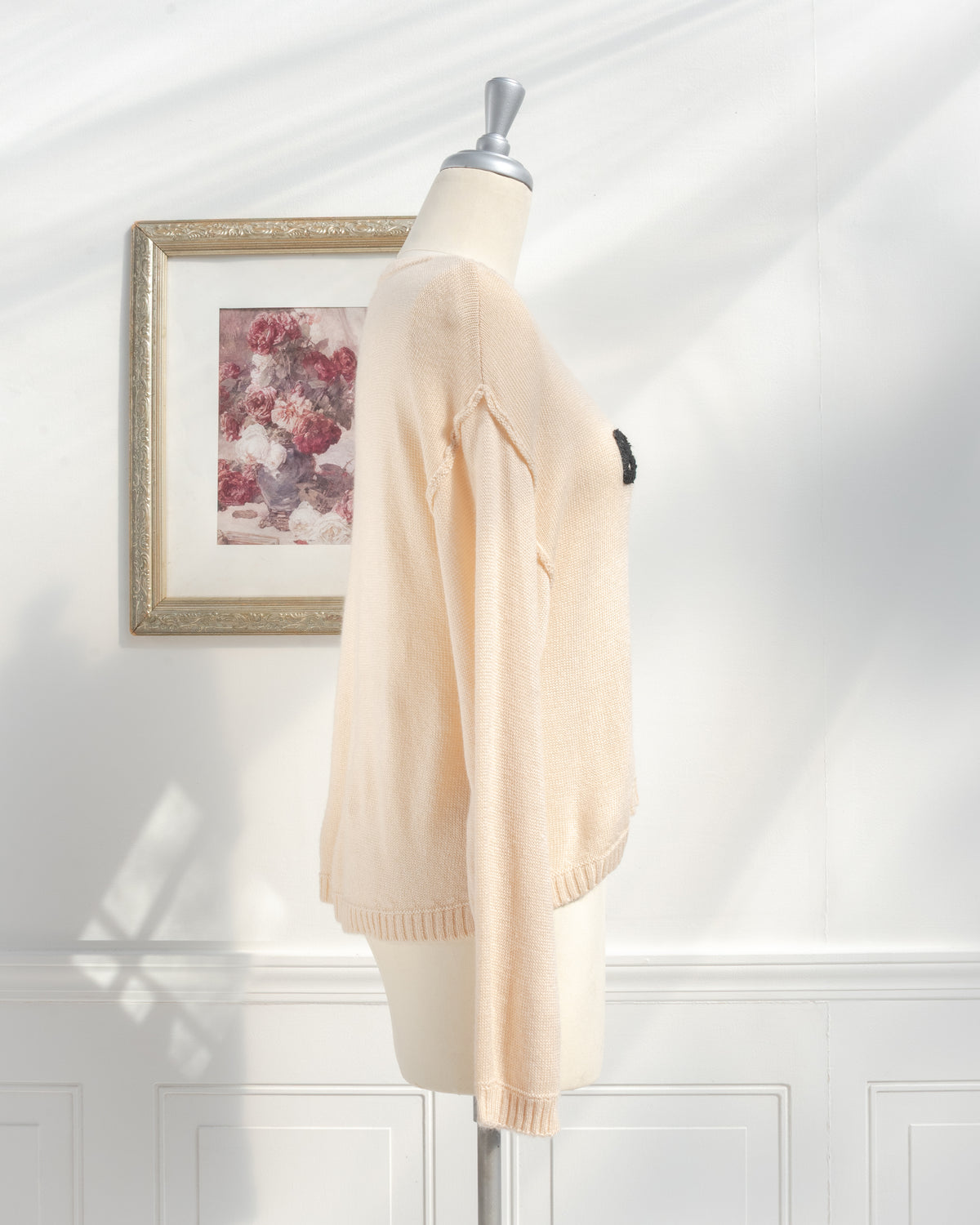 Beige knit sweater with relaxed drop shoulder and ribbed cuffs on a mannequin, classic style, side view.