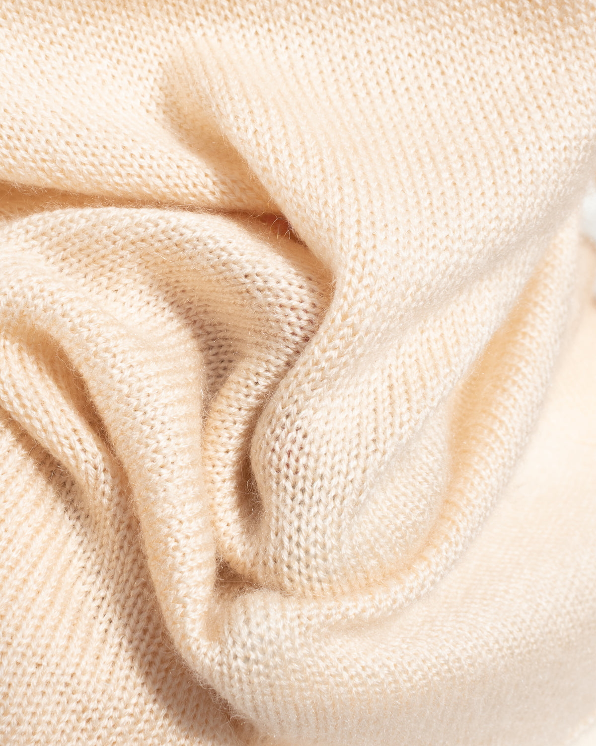 Beige knit sweater fabric draped in soft folds, texture detail view.