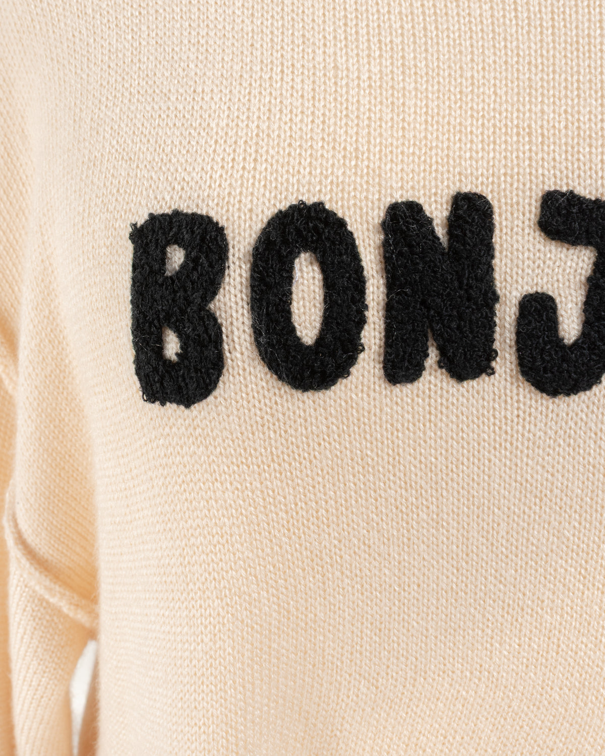 Beige knit sweater with raised black Bonjour appliqué, close up detail view.