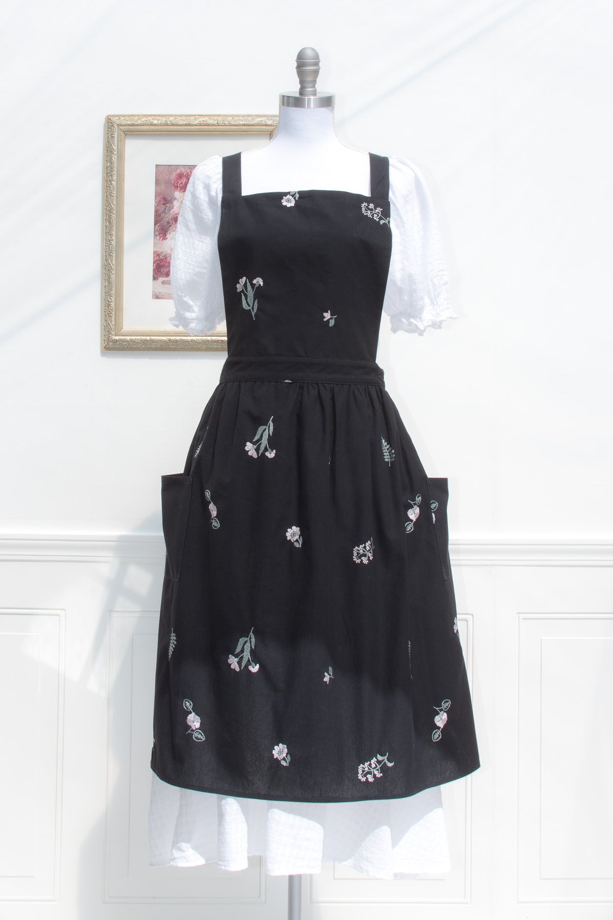 Black apron with scattered floral embroidery and front pockets shown from the front.
