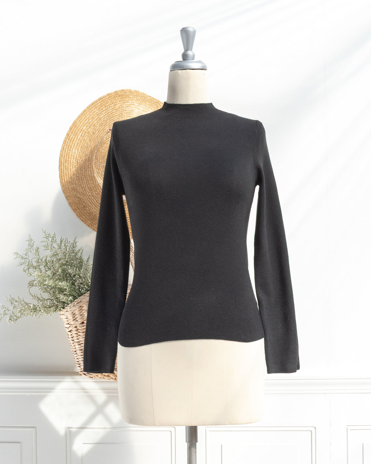 Black knit top with mock neck and long sleeves on a mannequin, French girl style, front view.