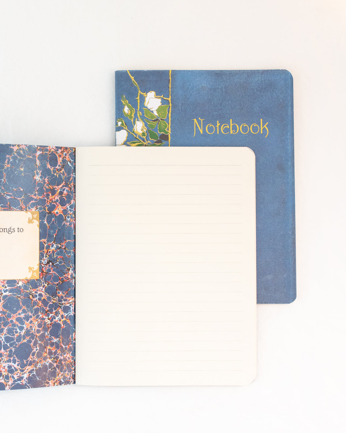 Open blue vintage notebook with marbled endpaper and a lined page beside the white rose cover, overhead flat lay view.
