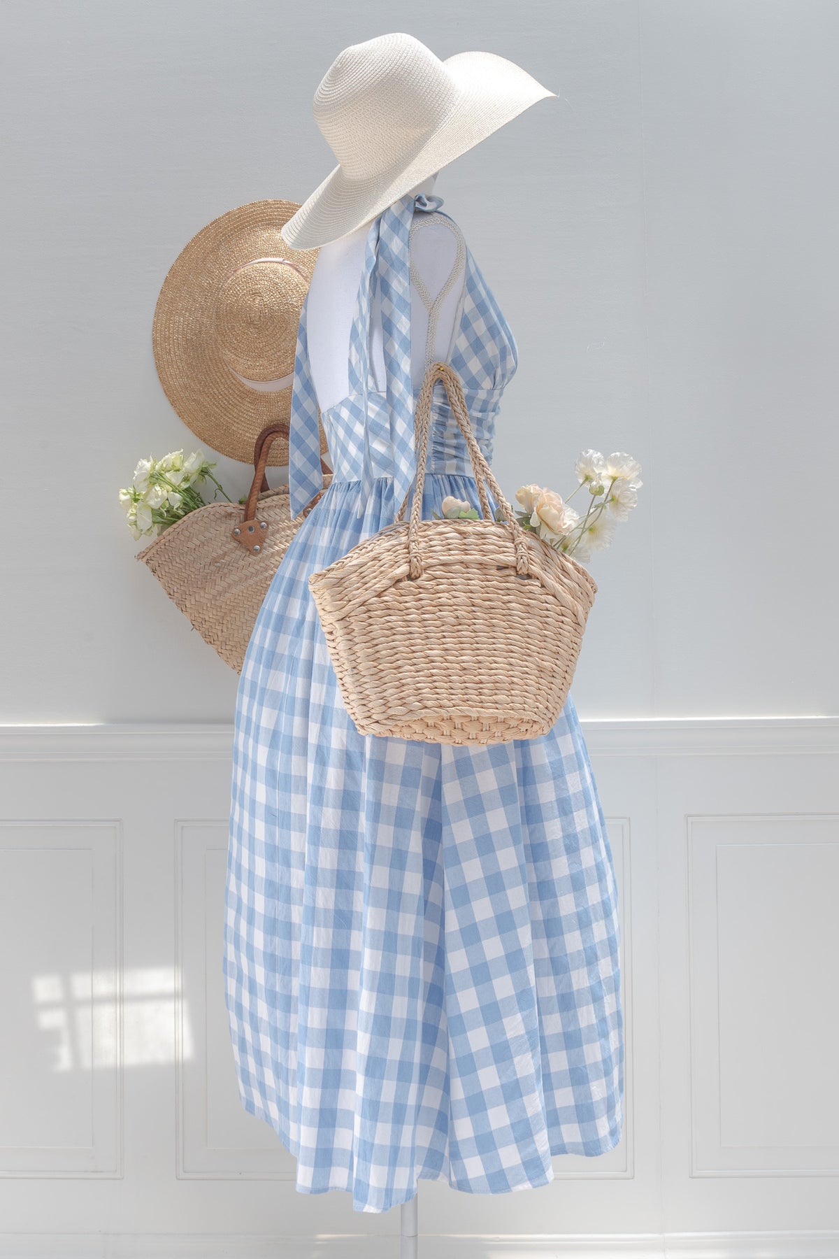 Blue and white gingham midi dress styled with woven bags, three-quarter view.
