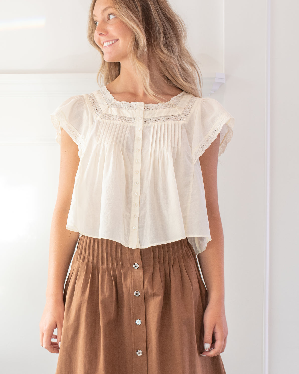Brown cotton midi skirt with button front and pleated waist, a feminine fall look, model close view.