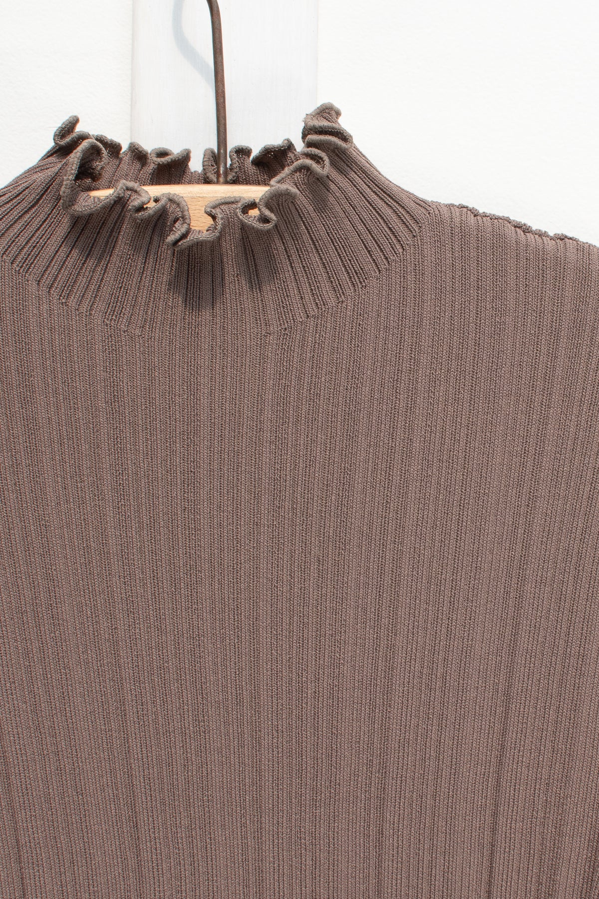 Detail of the lettuce-edge mock neck on the brown ribbed knit top.