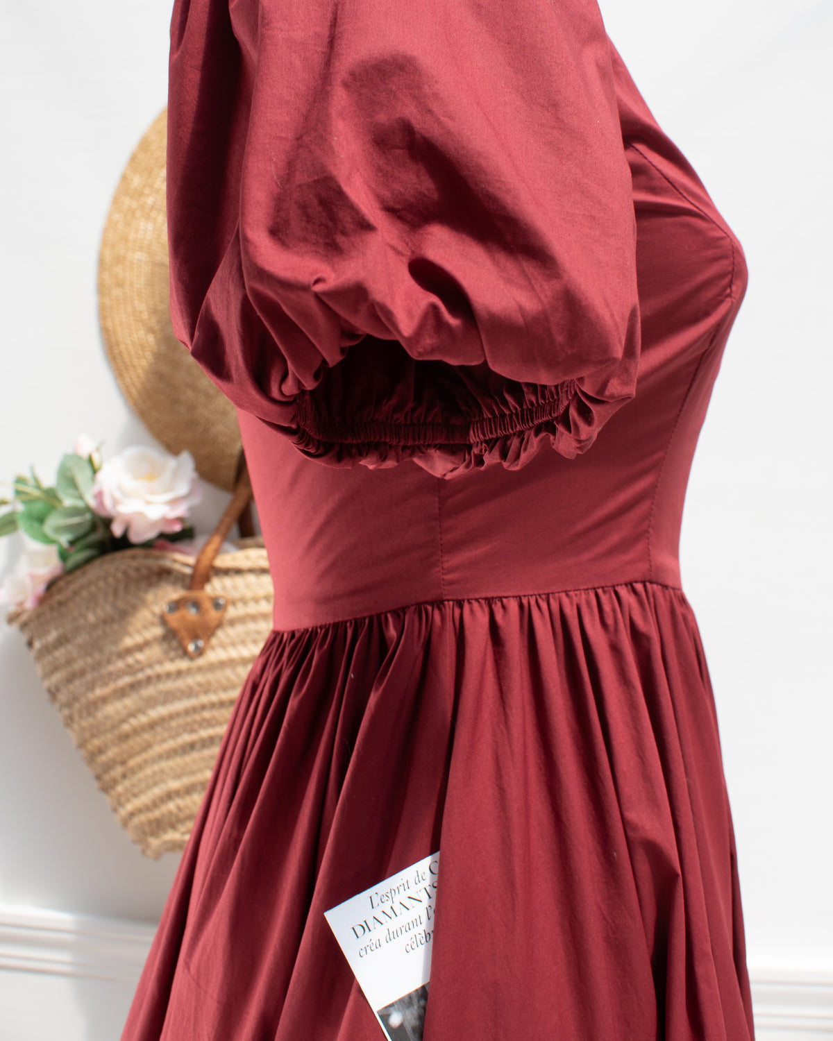 Close-up of the Felicity Dress puff sleeve with elastic cuff, gathered waist seam, and side pocket in burgundy cotton poplin.