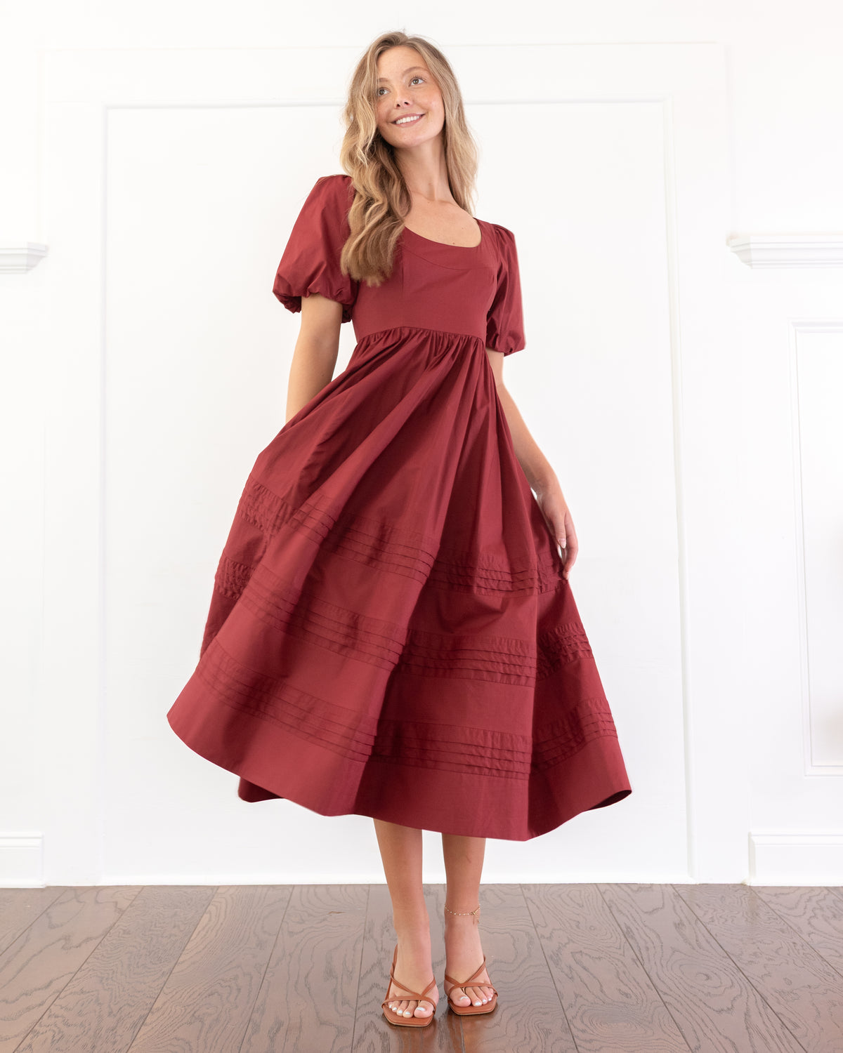 Woman twirling in the Felicity Dress, a romantic burgundy cotton midi dress with a full skirt and rows of pintuck detailing.