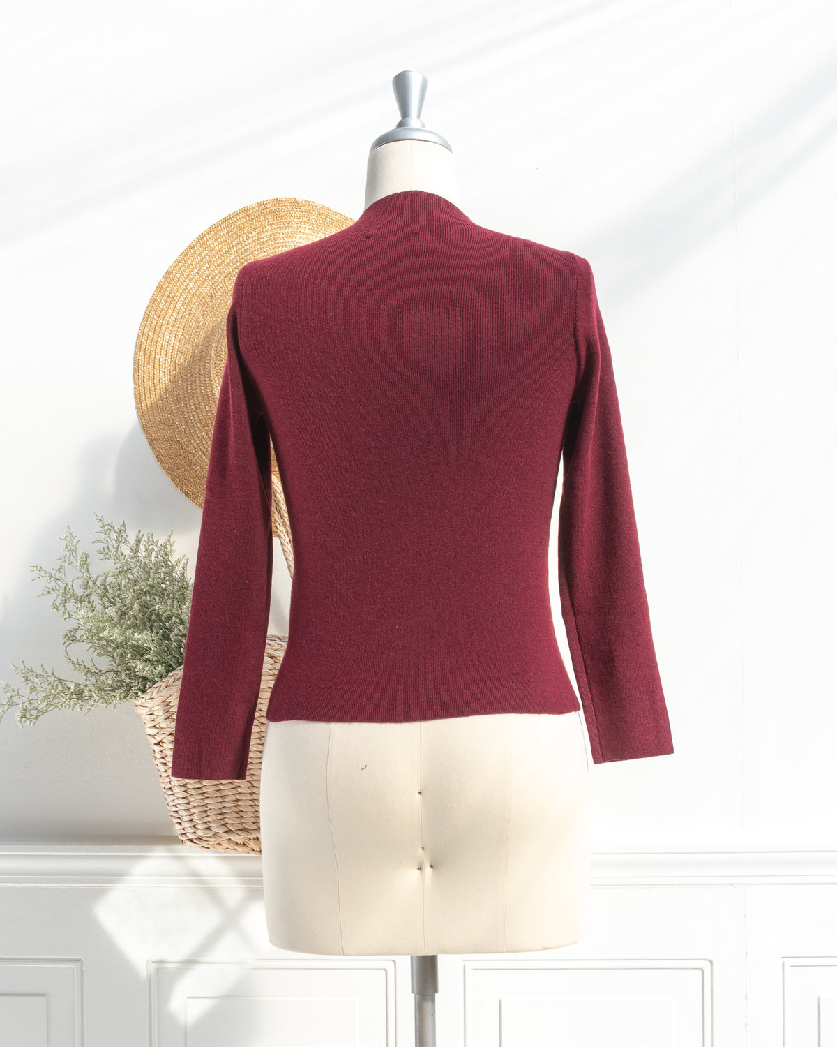 Burgundy knit top with clean silhouette and long sleeves on a mannequin, back view.