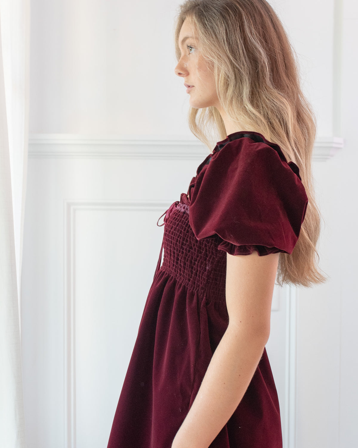Burgundy velvet mini dress with a smocked bodice and puff sleeve with a ruffle cuff, side detail view.