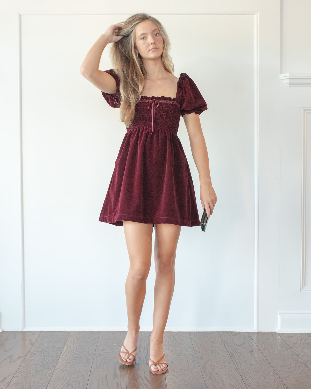 Burgundy velvet mini dress with a ribbon tie neckline styled with heels and a clutch, classic fall season, front view.