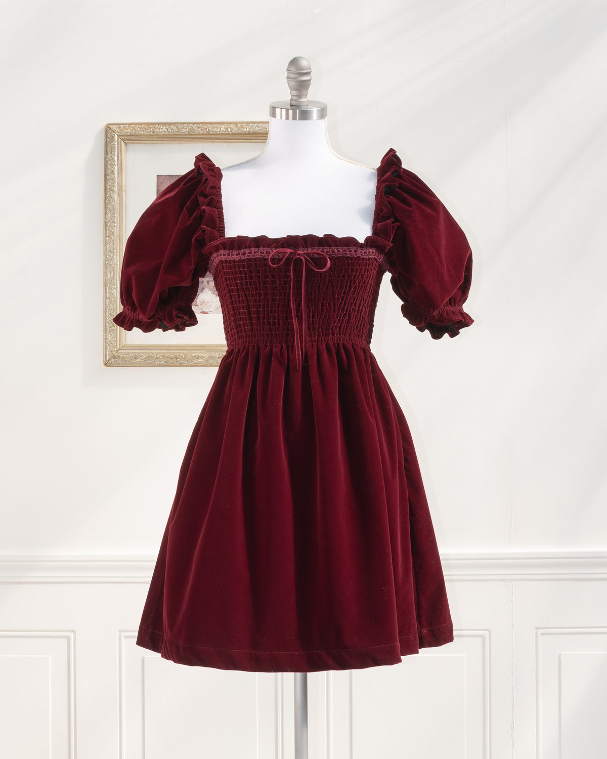 Burgundy velvet mini dress with a smocked bodice and puff sleeves, French girl style. Mannequin front view.