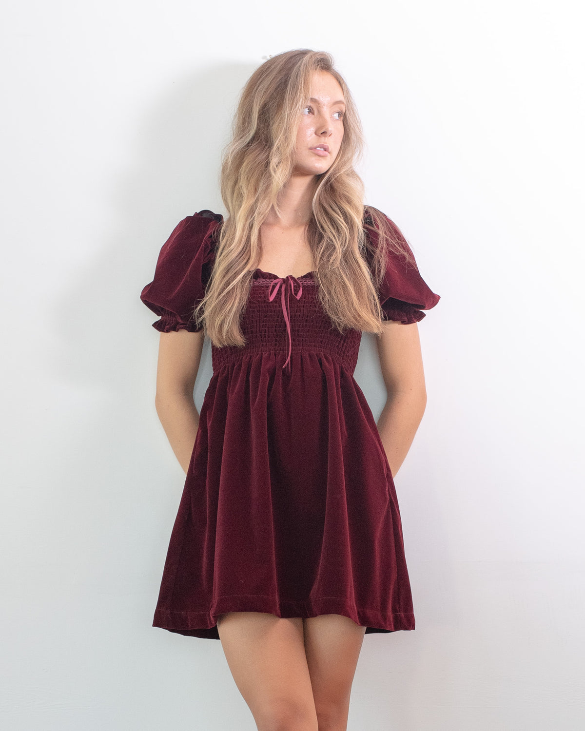 Burgundy velvet mini dress with a smocked bodice and puff sleeves, French girl style, worn by a model, front view.