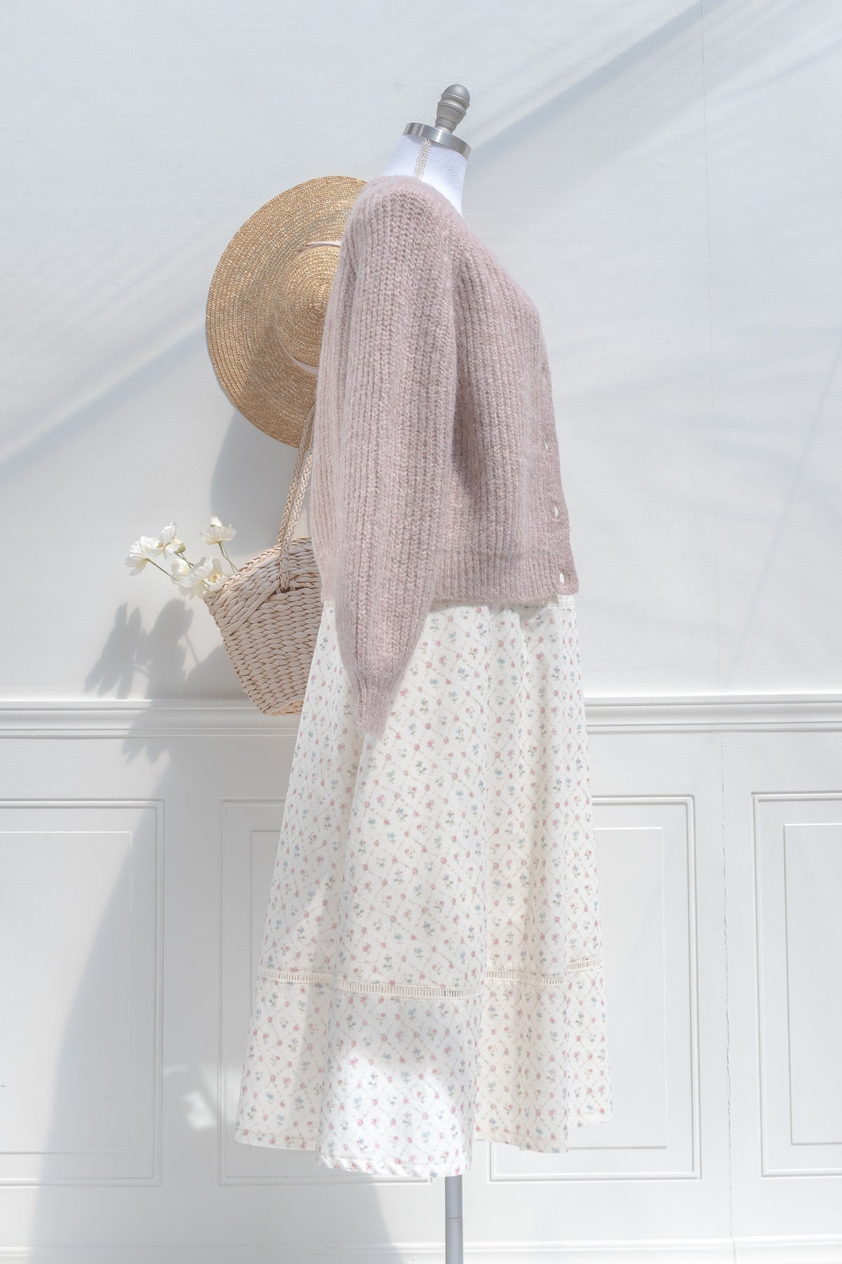 Mannequin wearing a pink knitted cardigan over a white dress against a white wall.