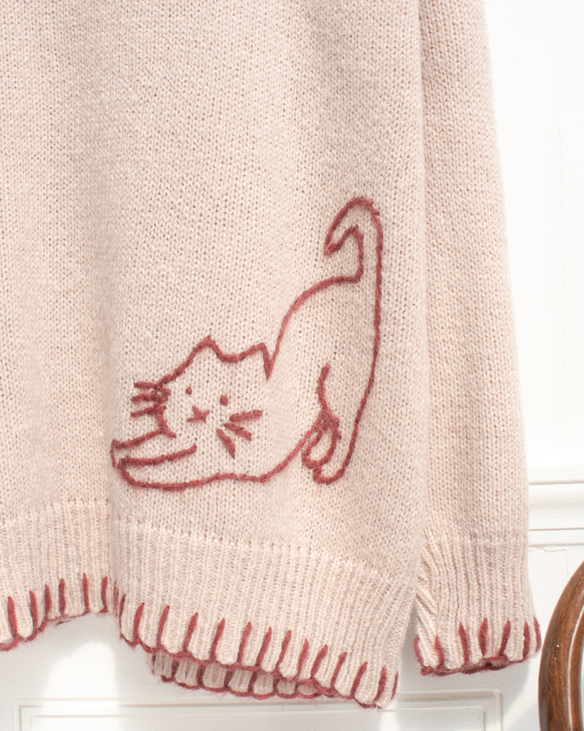 Blush knit cardigan with cat embroidery and maroon whipstitch hem, close detail view.