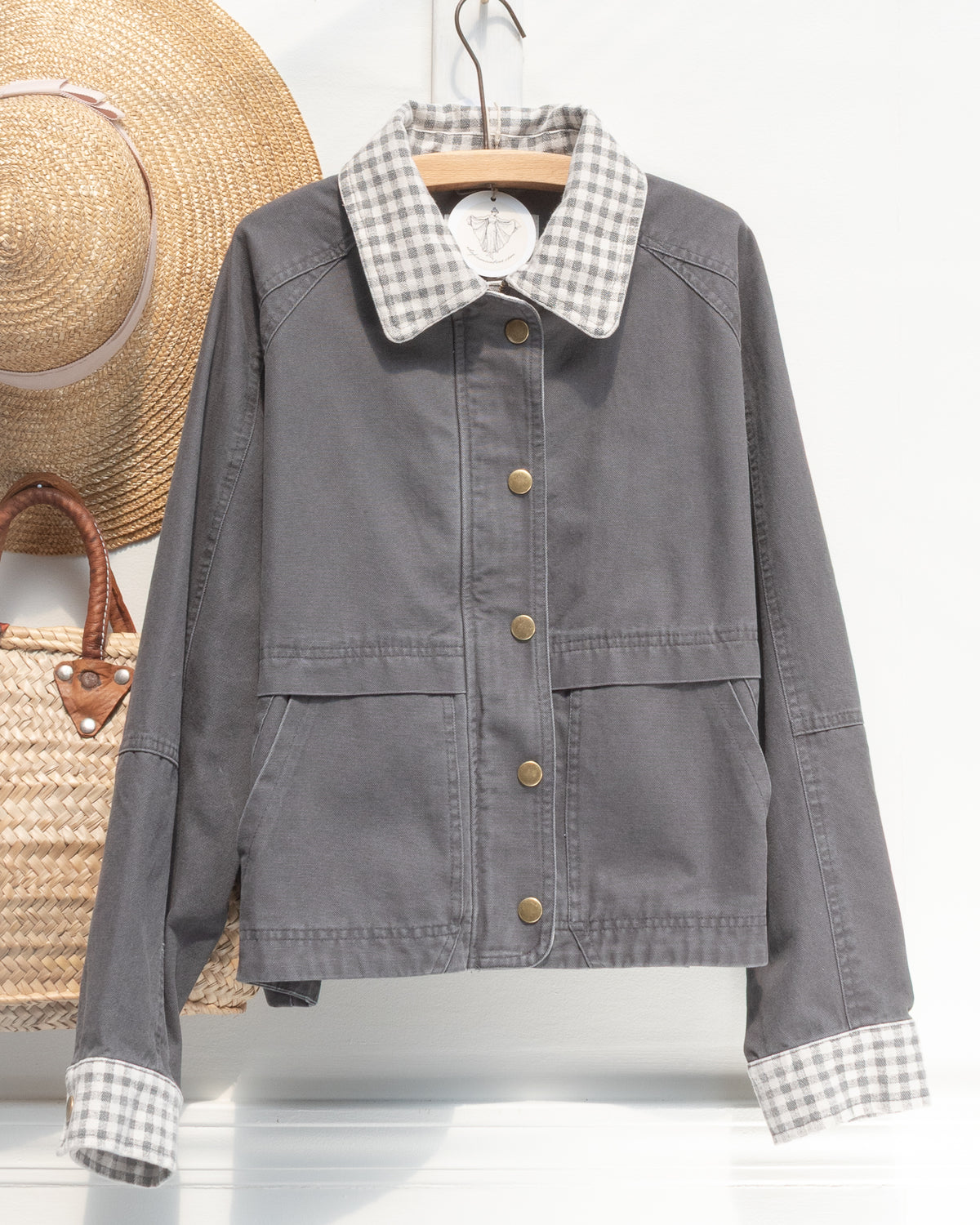 Charcoal cotton chore jacket with gingham collar and cuffs shown on a hanger, front view.