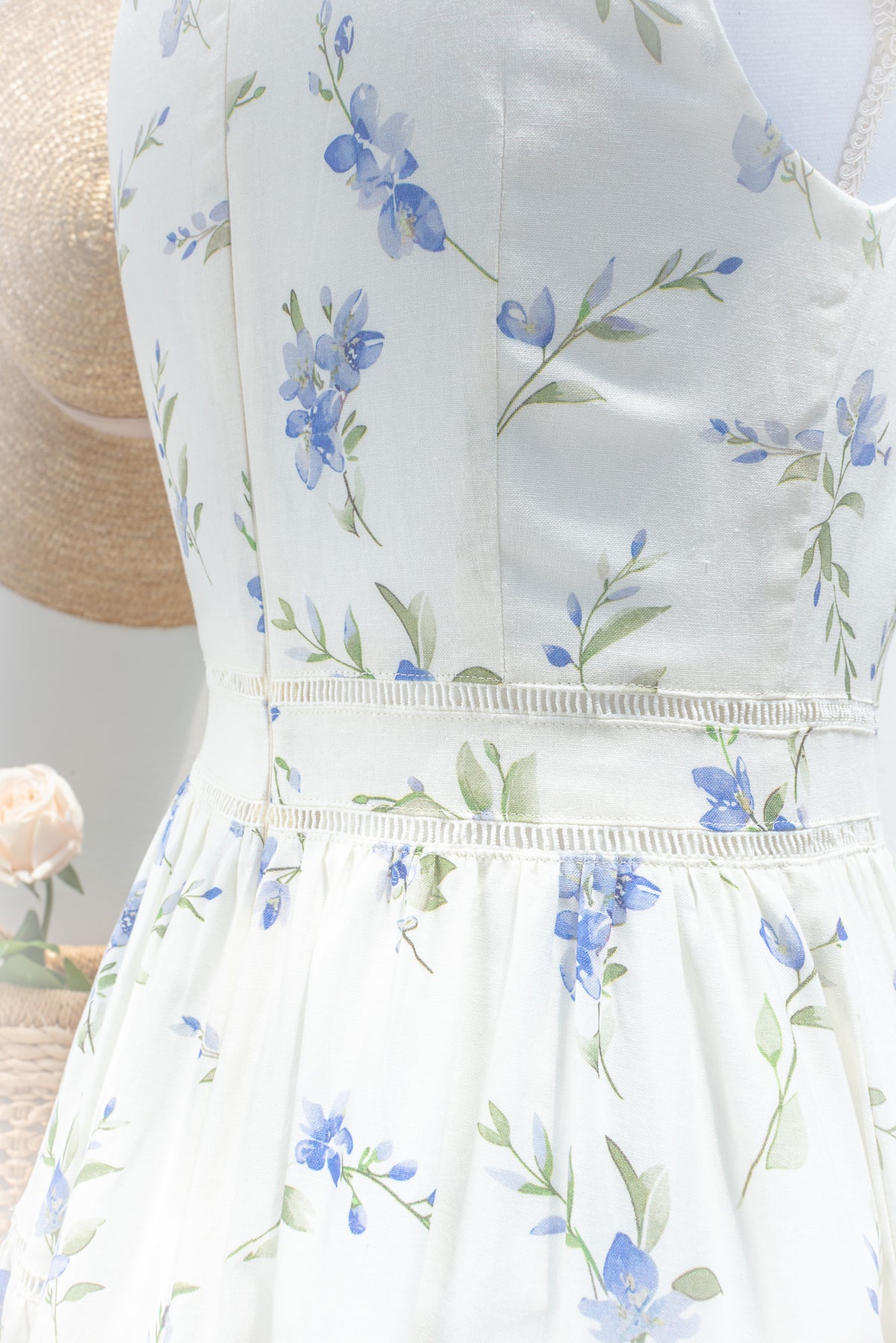 Feminine cream cotton fabric with blue floral and green leaf print and lace trim detail close up.