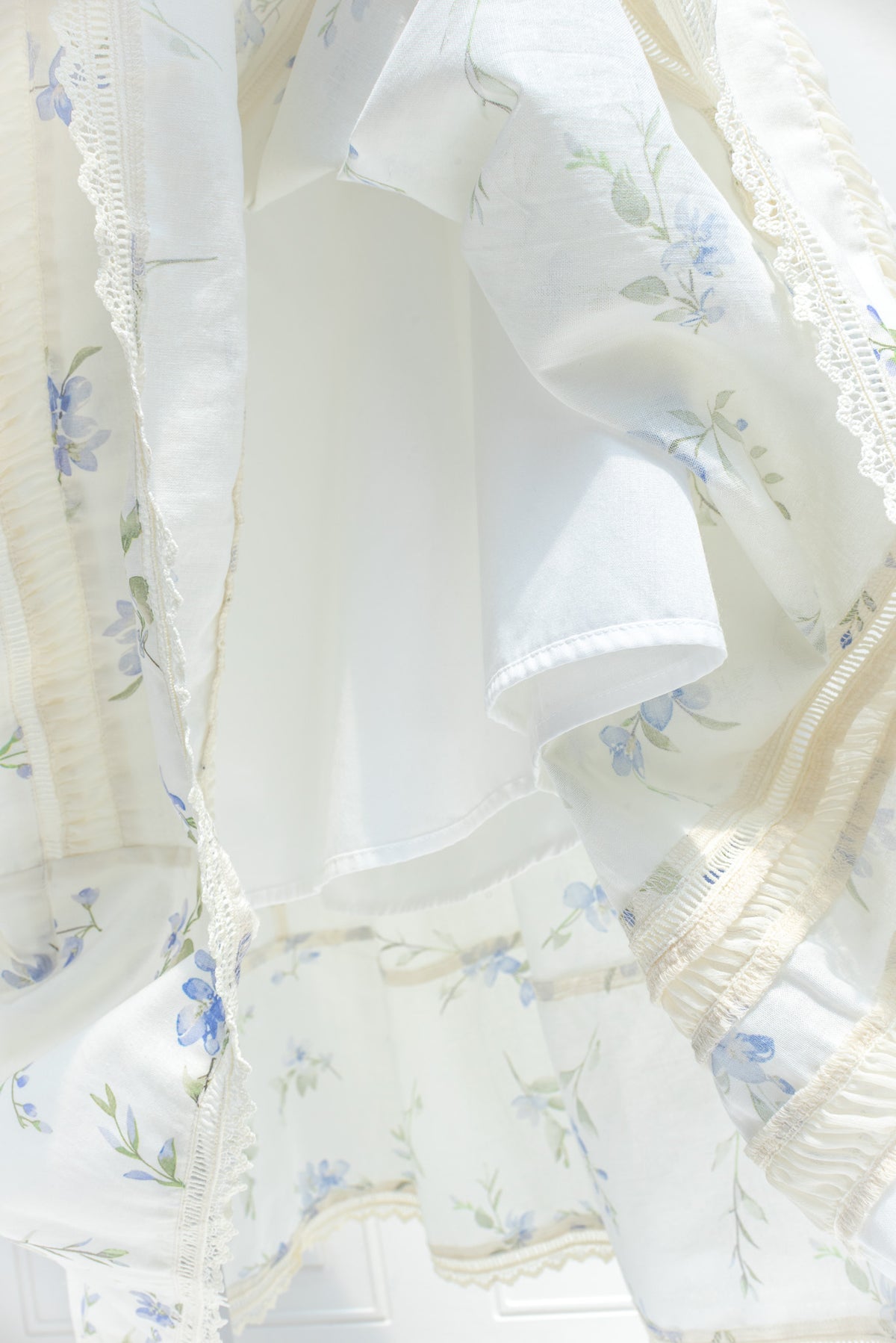 Cream cotton fabric with floral print and ladder lace trim detail close up.
