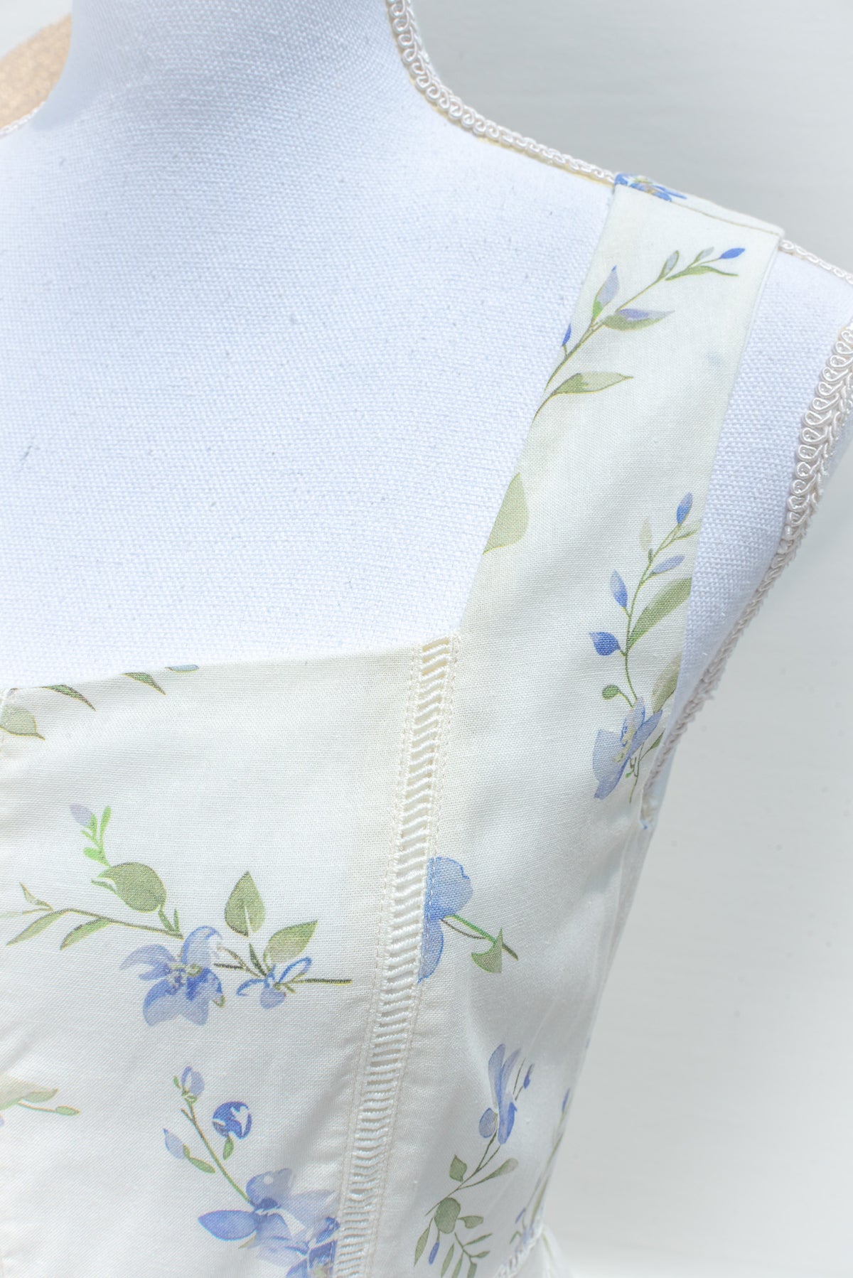 Cream cotton fabric with blue floral and green leaf print and lace trim detail close up.