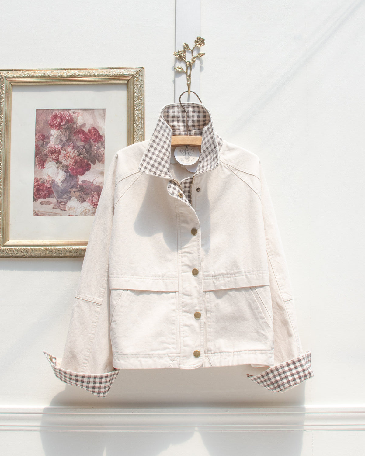 Cream cotton chore jacket with gingham collar and cuffs shown on a hanger, front view.