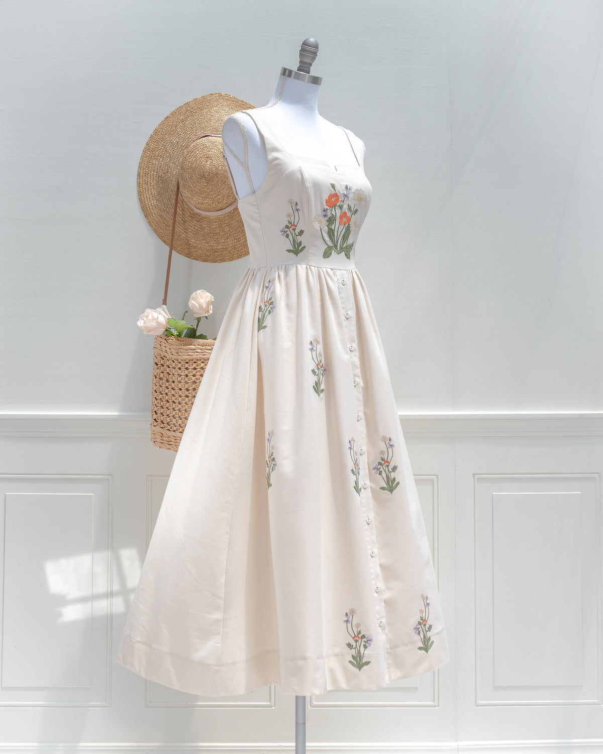 Three-quarter view of the cream embroidered midi dress, with a gathered waist, buttons down the skirt and floral embroidery.
