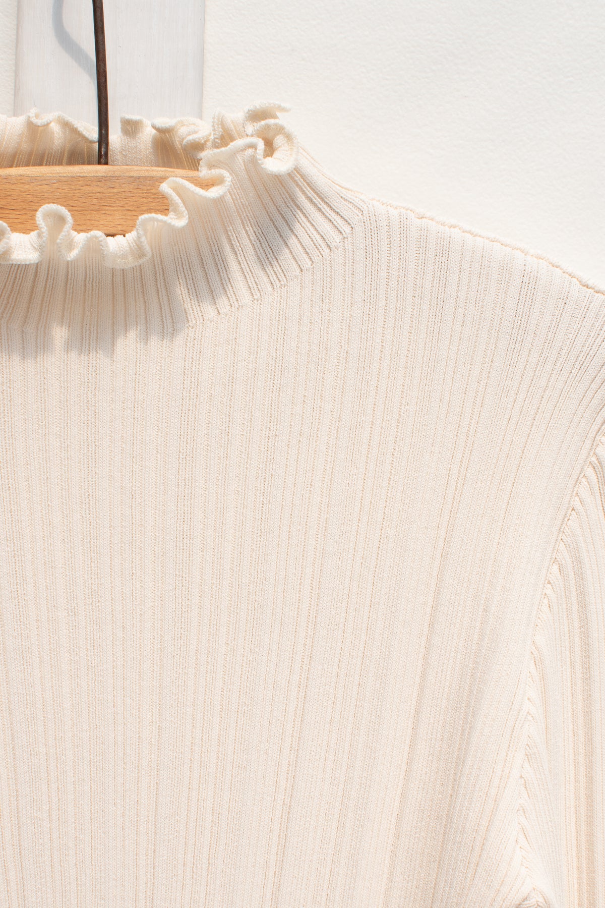 Detail of the lettuce-edge mock neck on the cream ribbed knit top.