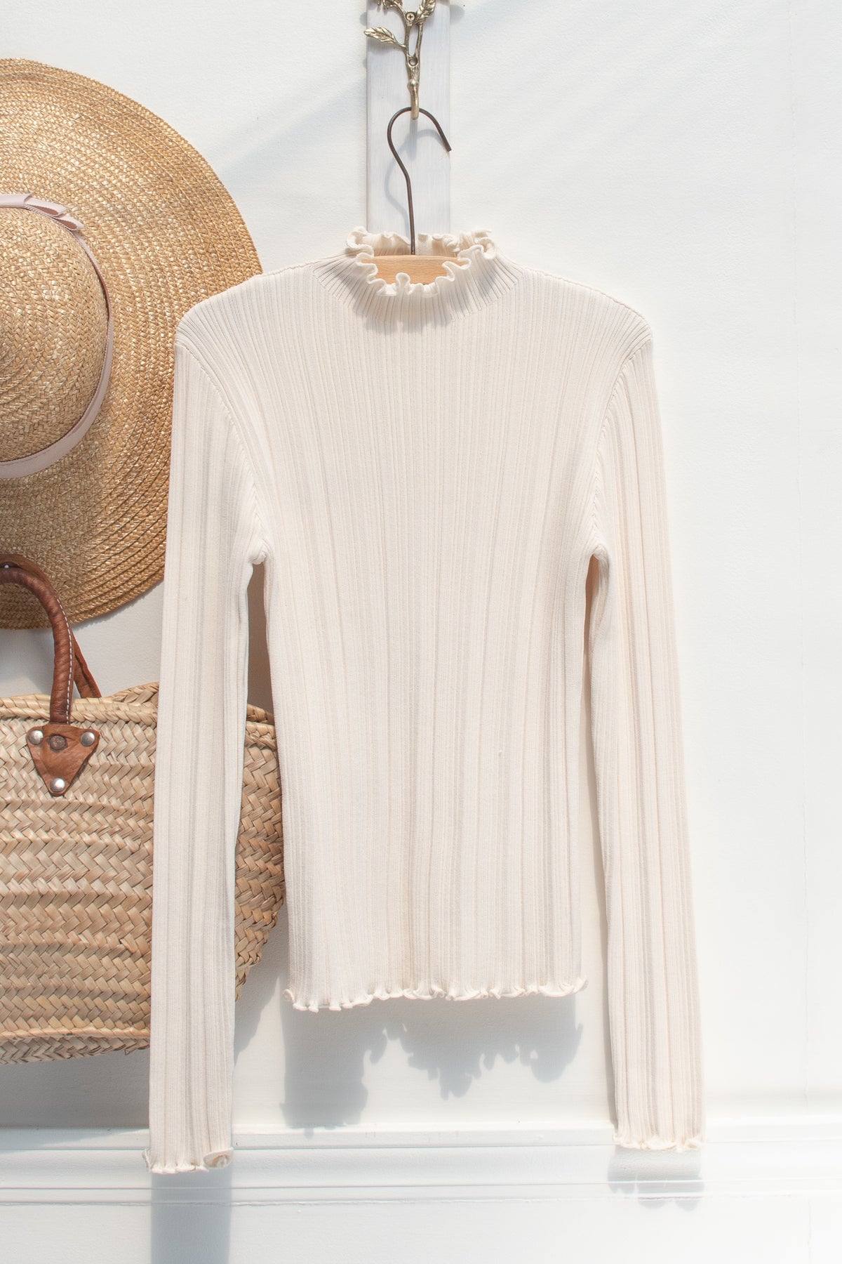 Cream ribbed knit top with a lettuce-edge mock neck, a wardrobe staple displayed on a hanger, front view.