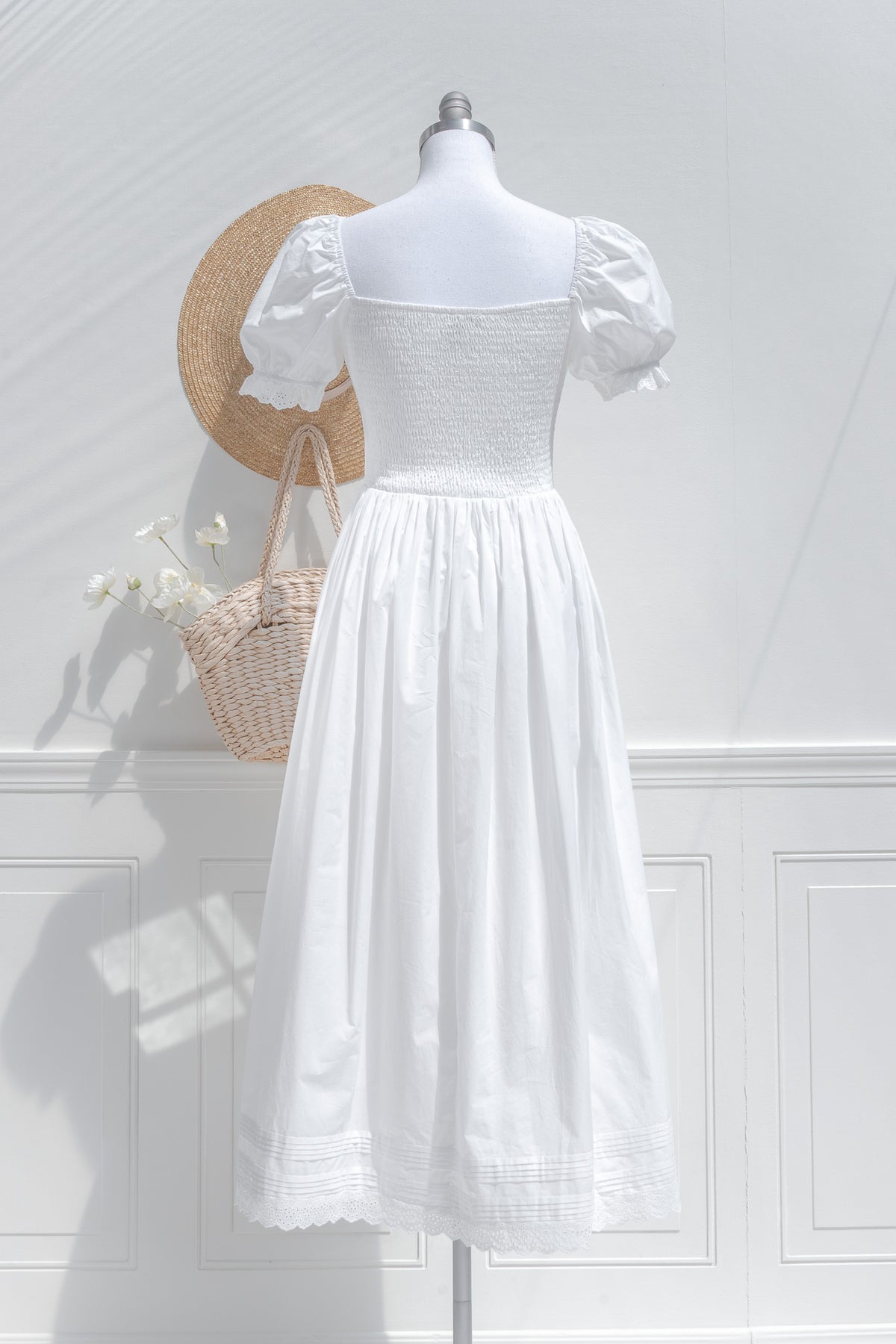 White dress on a mannequin against a white wall with a basket of flowers.