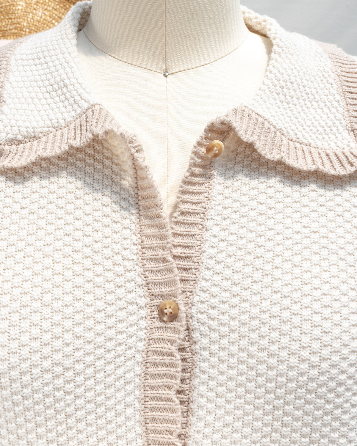 Ivory knit cardigan with tan trim along the scalloped collar and button placket, close mannequin view.