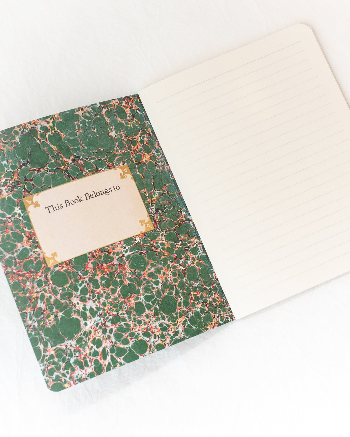 Open green vintage notebook showing green marbled endpaper, a name label, and a lined page, angled flat lay view.