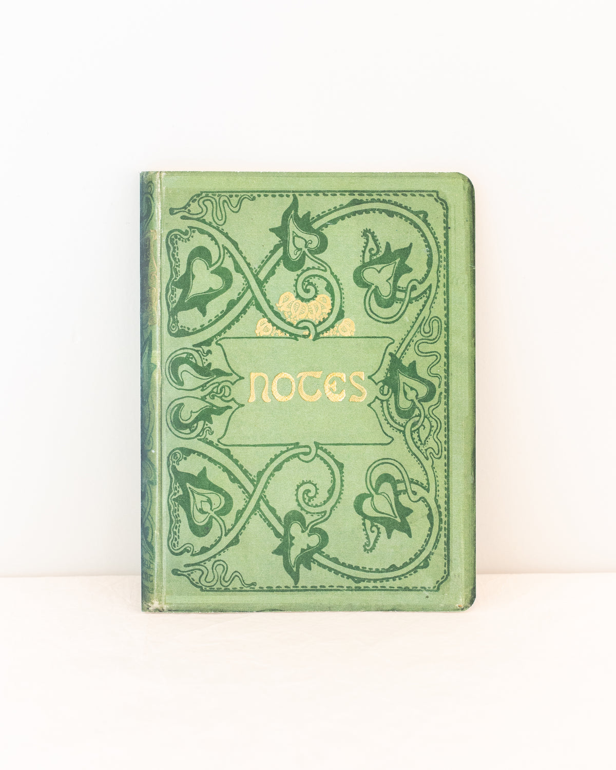 Green vintage notebook with an ornate vine cover and gold lettering that reads Notes, styled upright, front view.