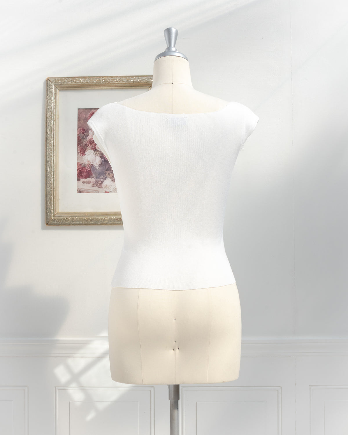 Ivory knit top with boat neckline and cap sleeves on a mannequin, back view.