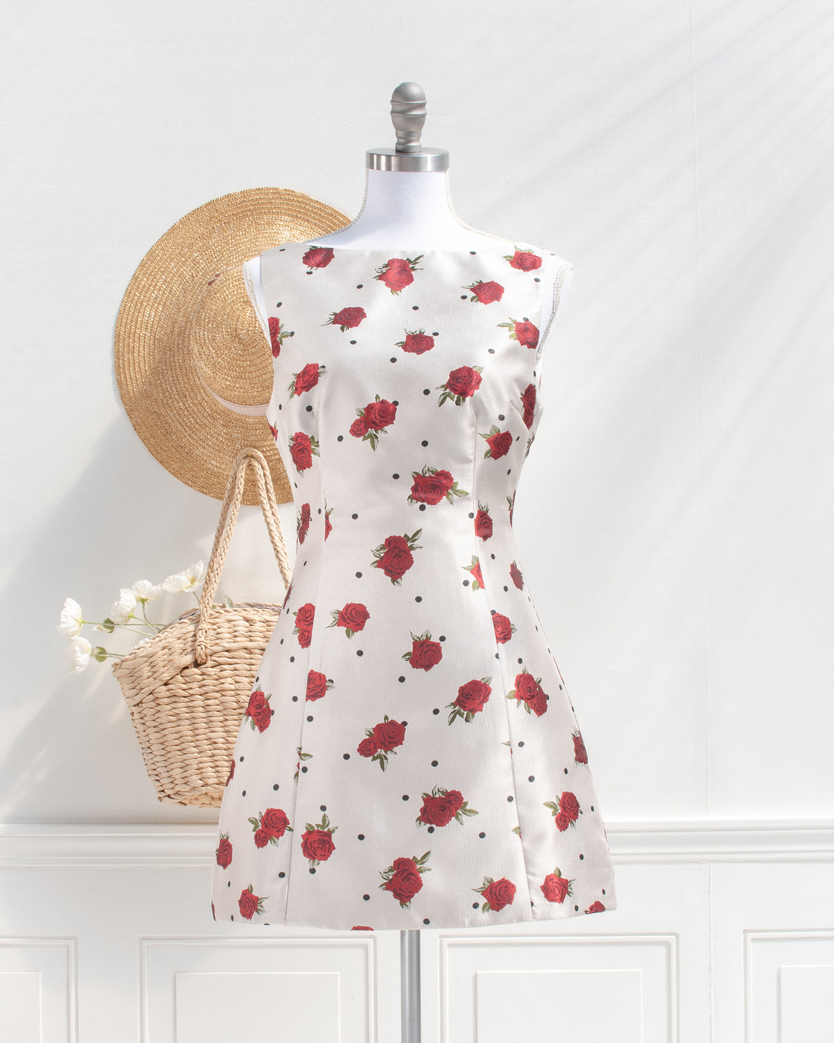 Ivory rose and polka dot mini dress with a boat neckline styled with a straw hat and basket, classic look, front view.