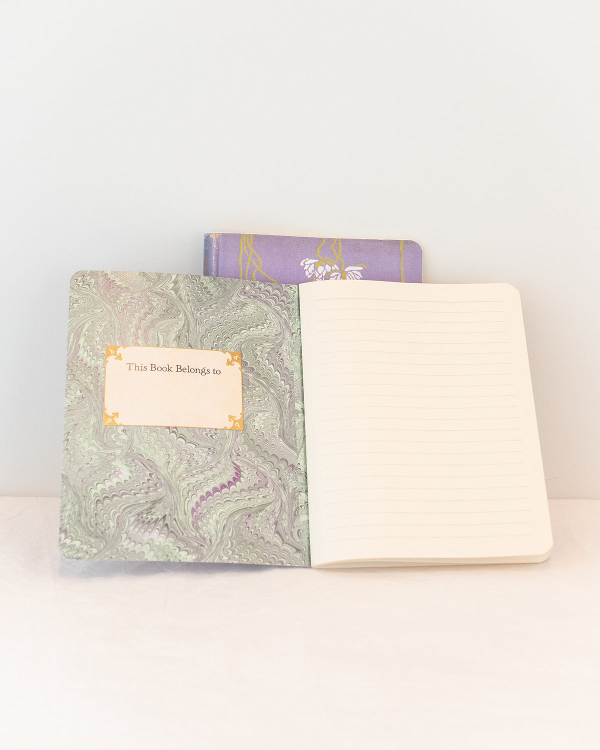 Open lavender vintage notebook showing sage green marbled endpaper, a name label, and a lined page, front view.