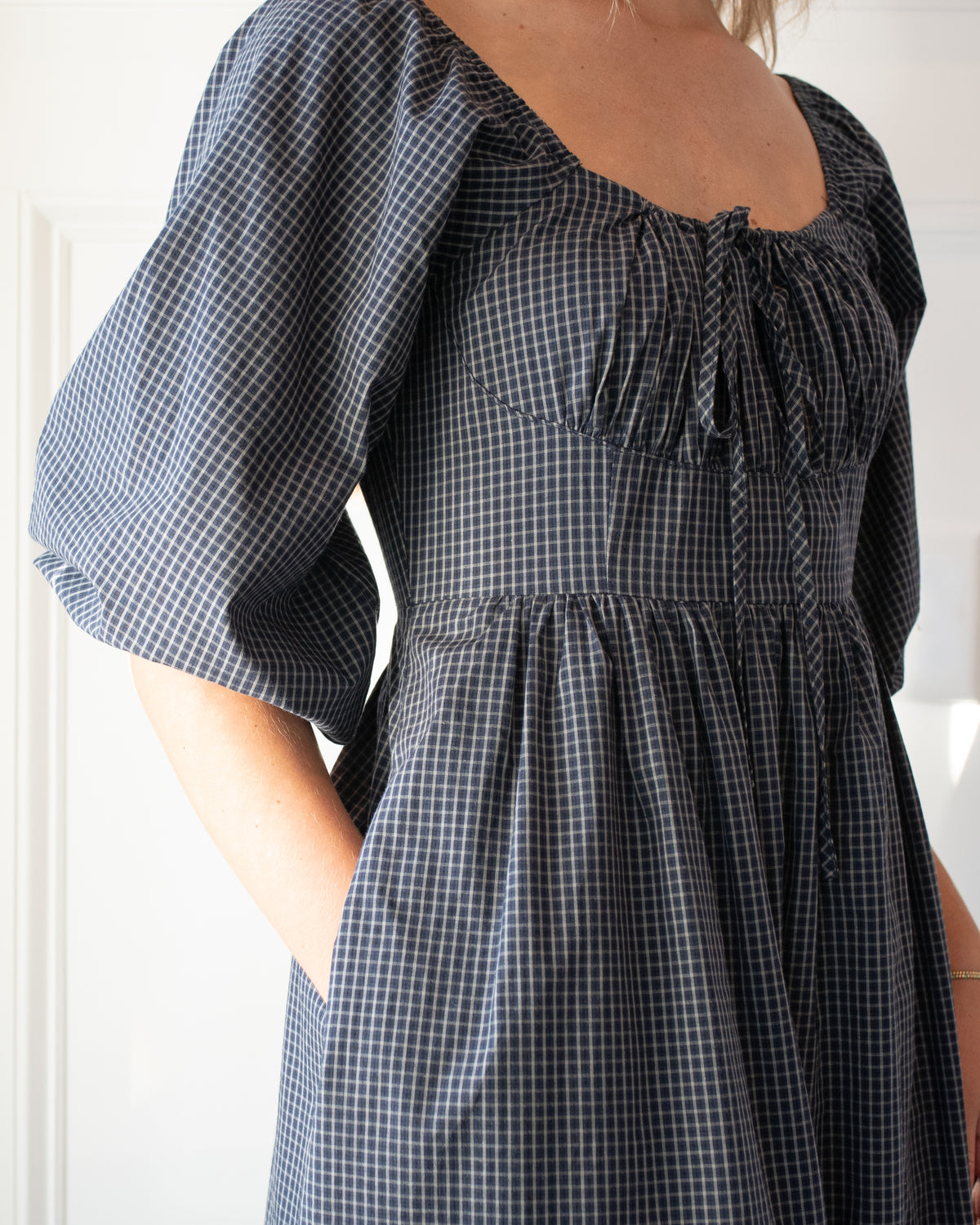 Navy check cotton midi dress with ruched bust and adjustable tie neckline, close model view.