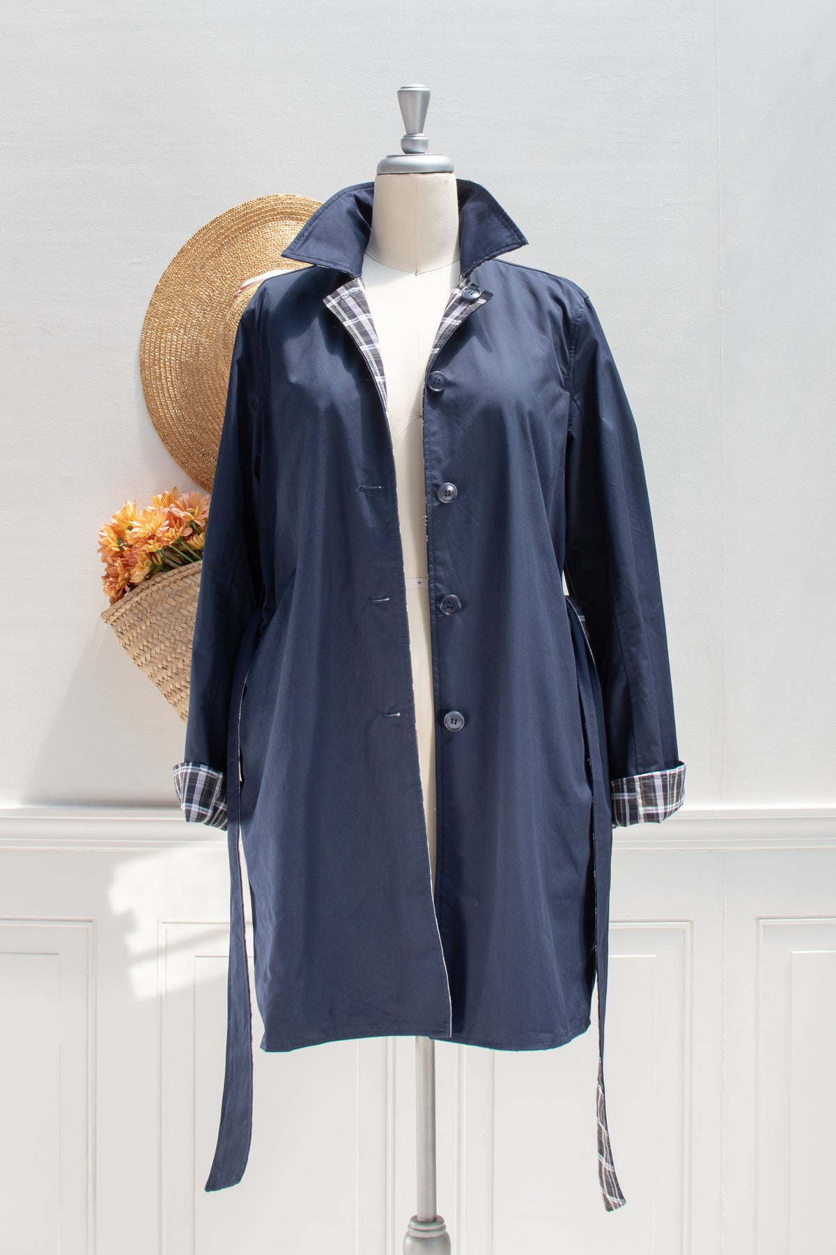Navy cotton reversible trench coat worn open with plaid trim on a mannequin, front view.