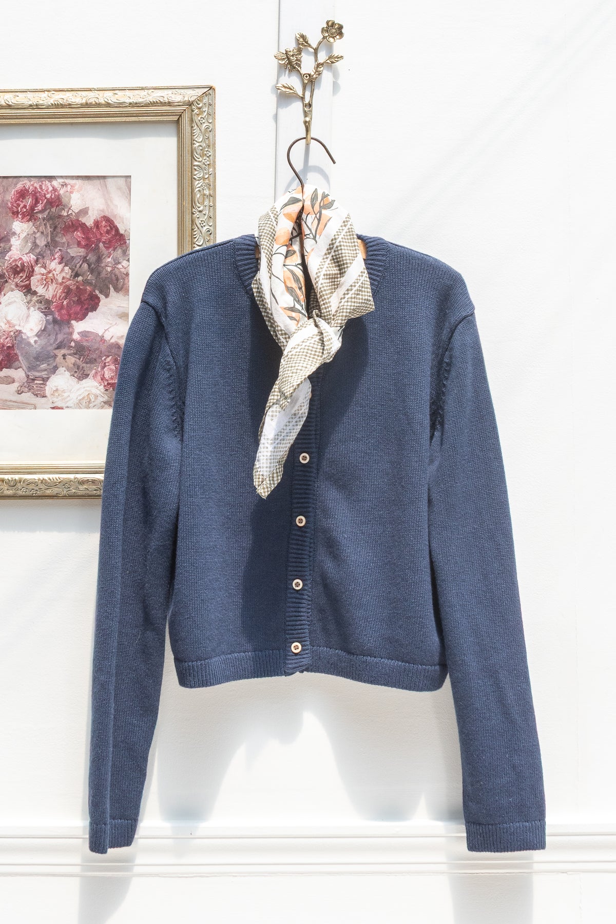 Navy cotton wool cardigan hanging on a hook with a floral scarf, front view.