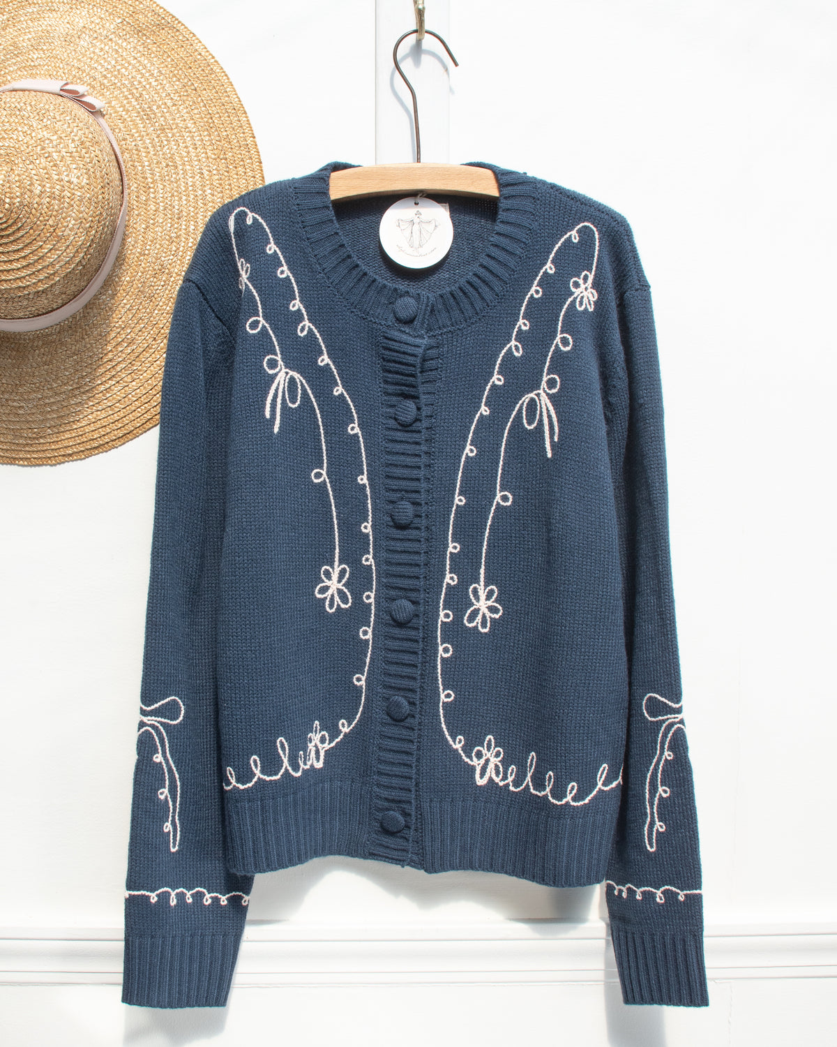 Feminine style cardigan. French girl style. Blue cardigan with whimsical bow detail embroidery. Hanger view. Amantine