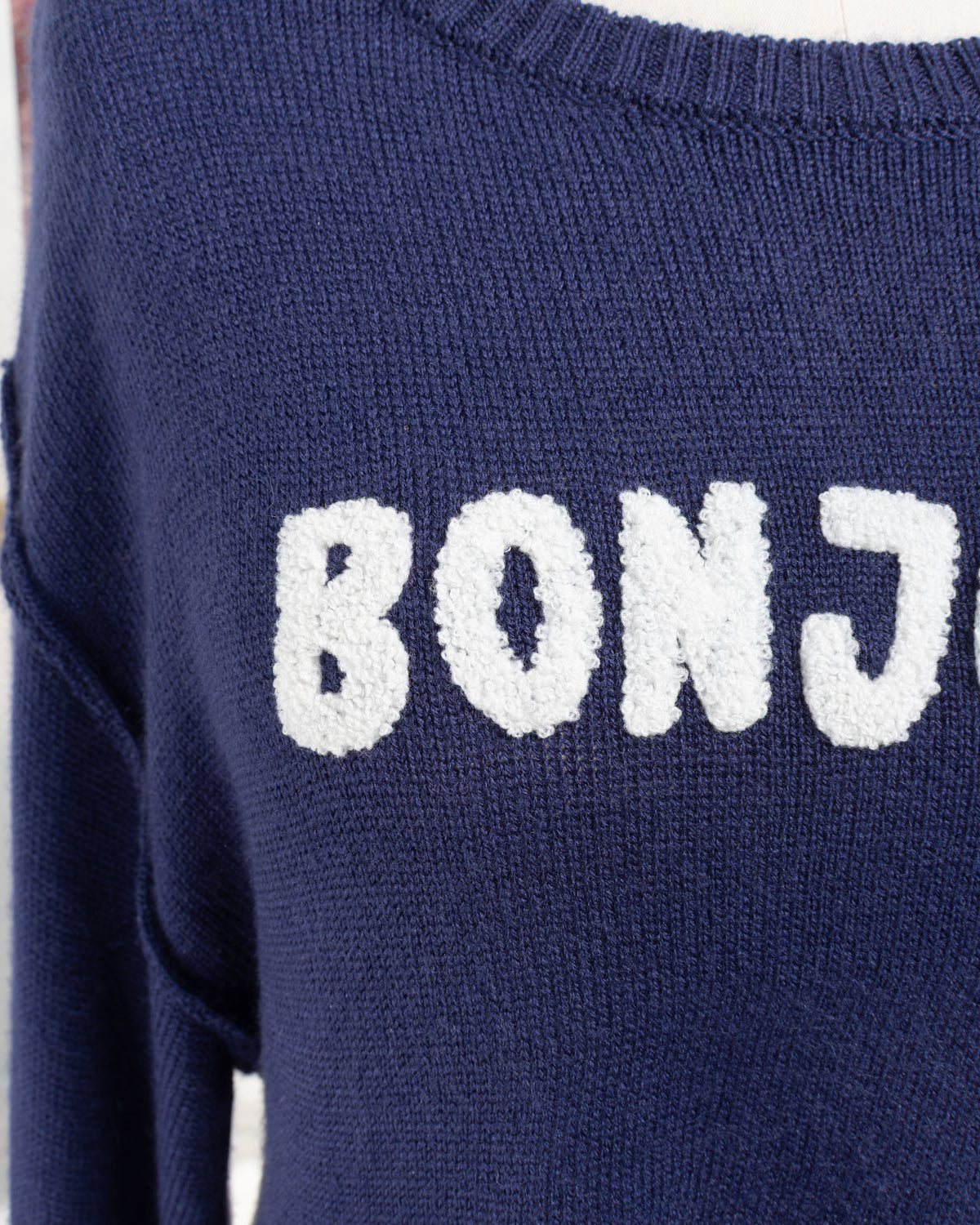 Navy knit sweater with raised white Bonjour appliqué, close up detail view.