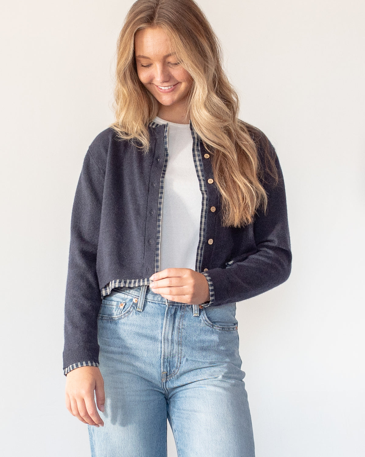 Navy knit cropped cardigan with plaid trim worn open over a white tee and denim, model front view.