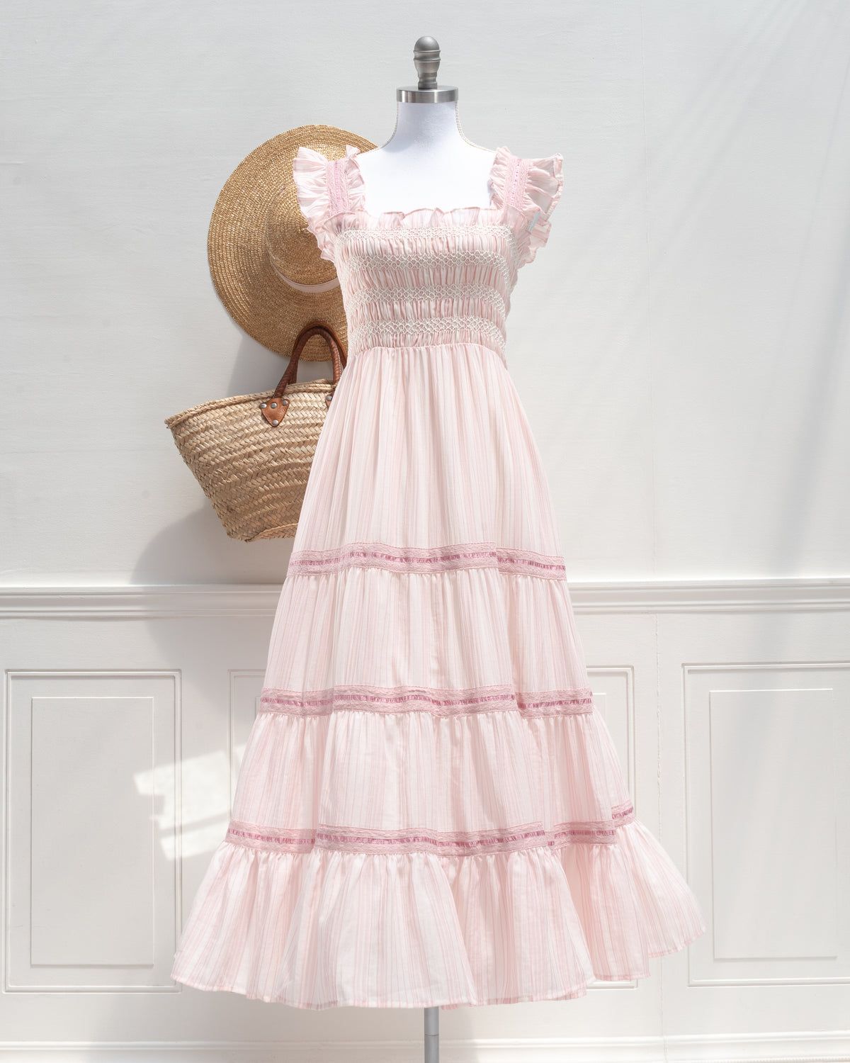 Blush pink striped midi dress with flutter sleeves and smocked bodice on a mannequin, feminine style, front view.