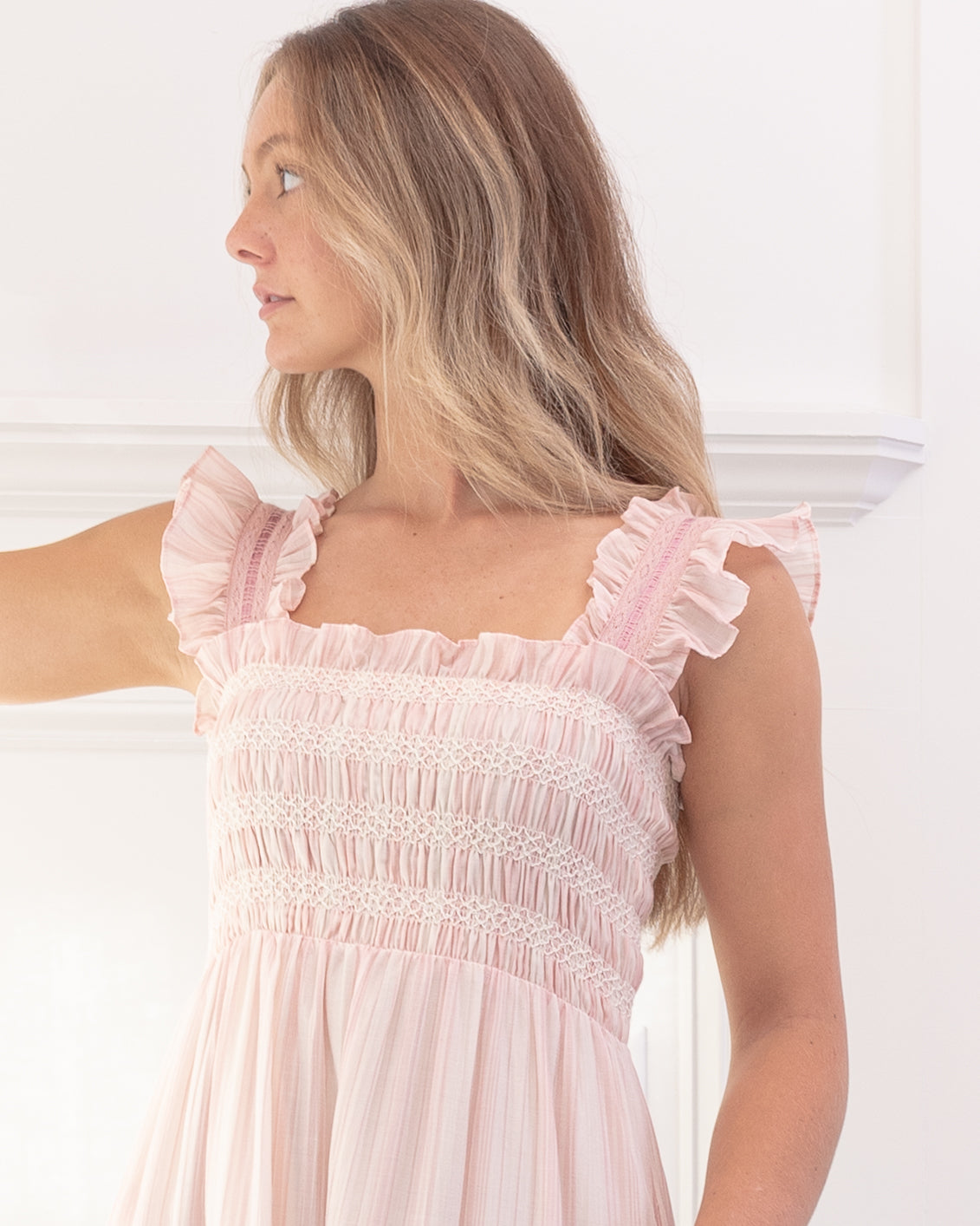 Blush pink striped dress with smocked bodice and flutter sleeves on a model, feminine romantic style, close up view.