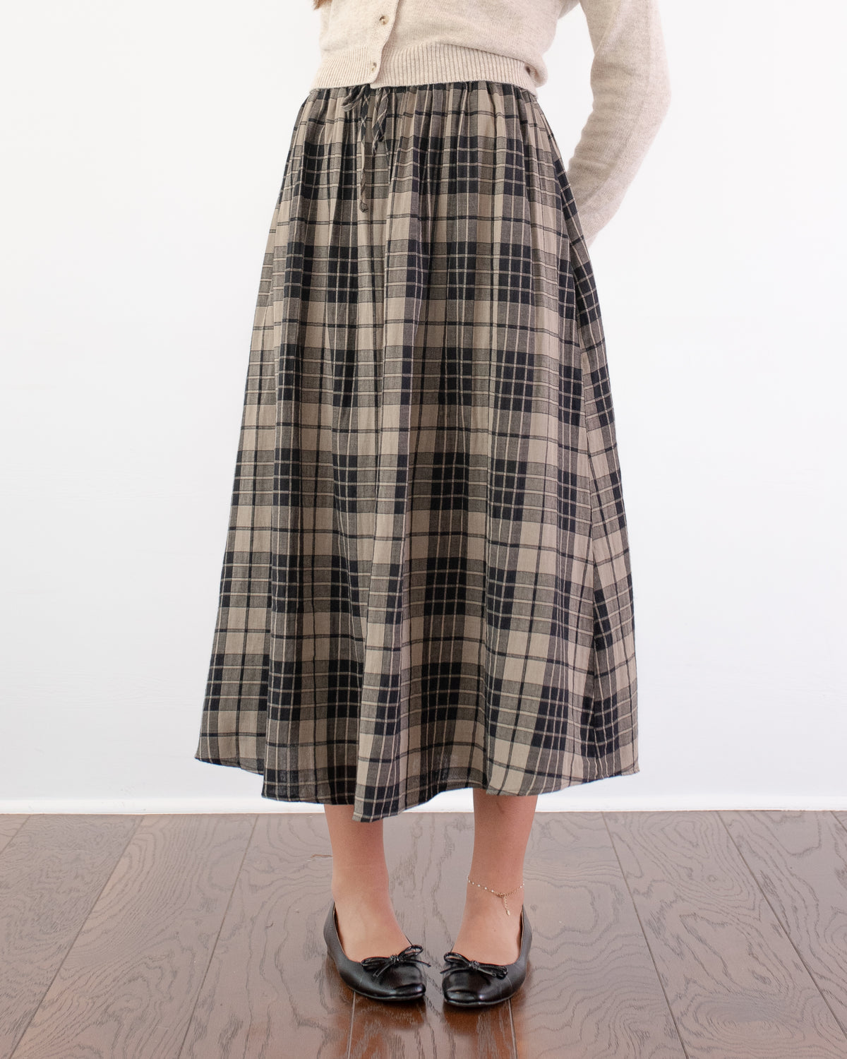 Tan and black plaid cotton midi skirt with gathered waist styled with ballet flats, model front view.