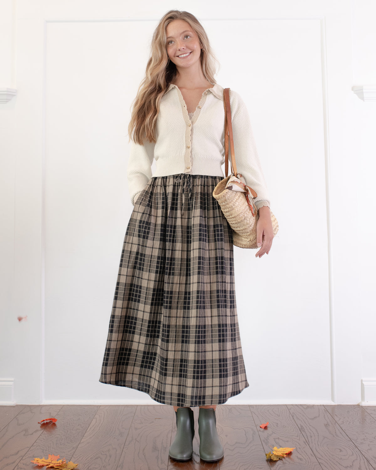 Tan and black plaid cotton midi skirt styled with a cream cardigan and boots, a classic fall look, model front view.