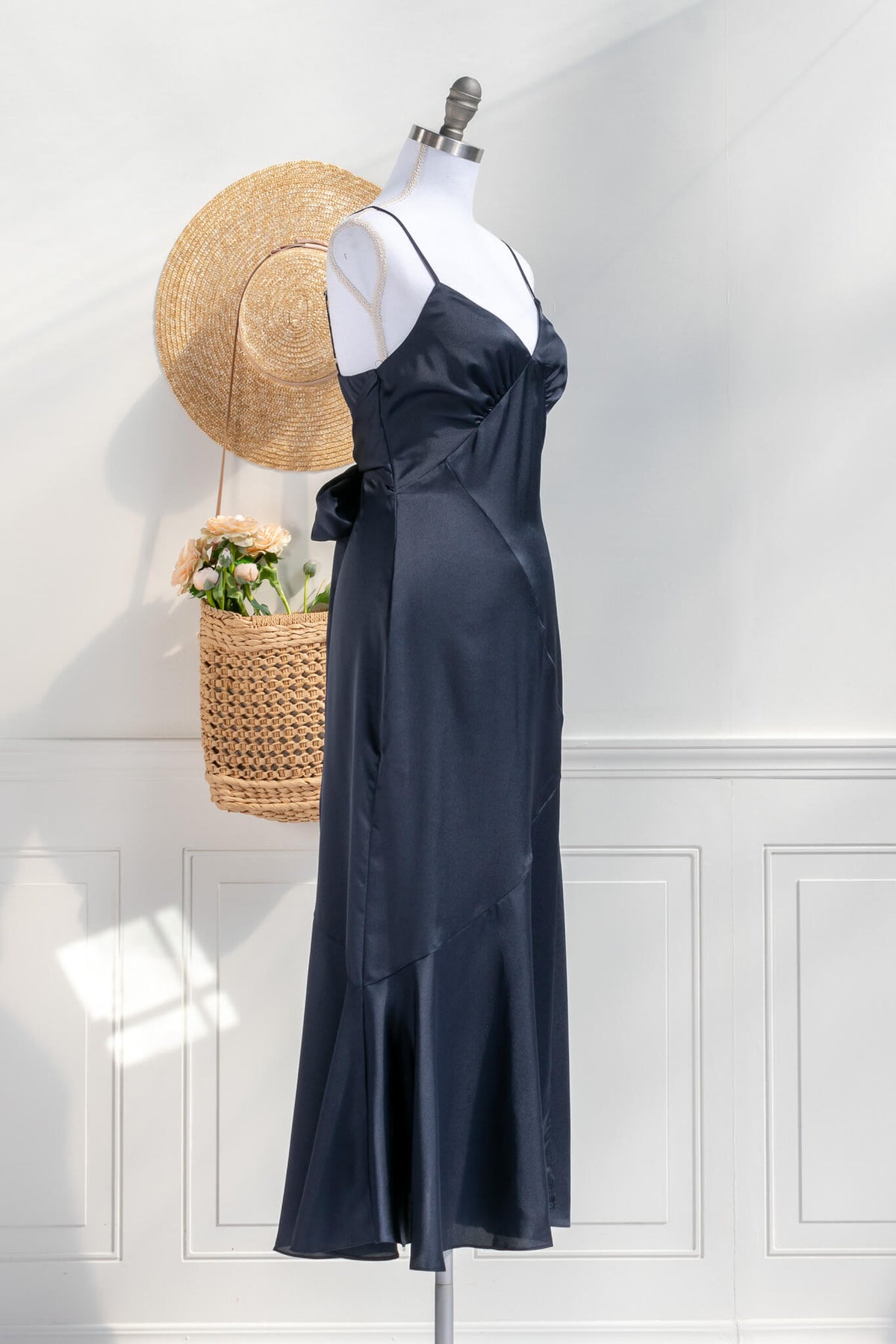 Beautiful wedding guest and formal dress in navy blue. French style feminine and romantic dress with straps, slit, and a bow. 3/4 side view. Amantine dresses.