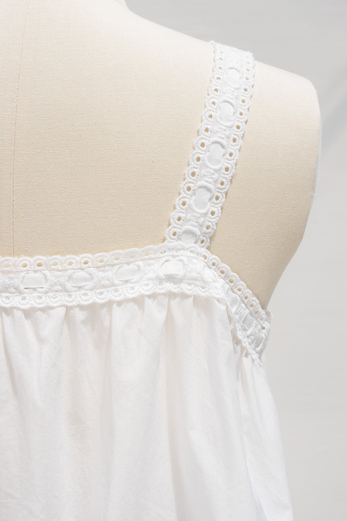 Close up of white cotton chemise top showing eyelet trimmed strap and gathered back detail.
