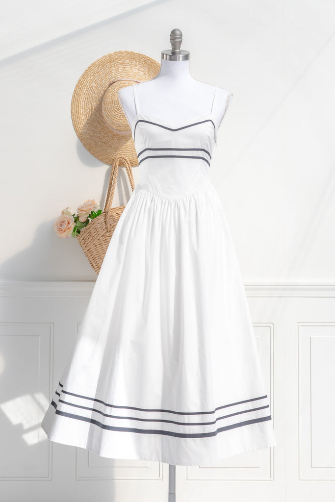 Cottagecore-inspired white summer dress with navy blue stripes, styled with a straw hat and a basket of roses, perfect for a serene day in the countryside.